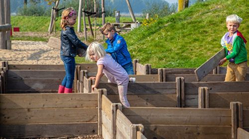 Kinderen bouwen een doolhof van houten planken in de speurtuin
